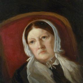 Head-and-shoulders painting of Sarah Austin by Lady Arthur Russell, c. 1867. She is leaning sideways in a red chair, wearing a white cap with lappets hanging down on each side, and a simple black dress with white collar. National Portrait Gallery.