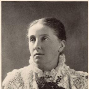 Black and white photograph of Ada Cambridge, shown from the shoulders up. Her head is turned slightly to the side, her hair is pulled back and she is wearing an intricately patterned lace dress.