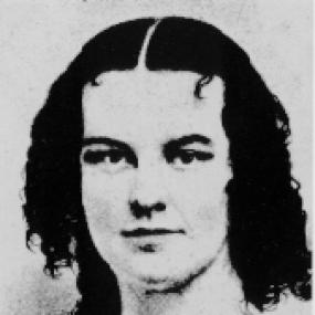 Black-and-white, head-and-shoulders photograph of Rebecca Harding Davis. She faces forward, her dark hair parted severely straight down the middle and curling on her shoulders.