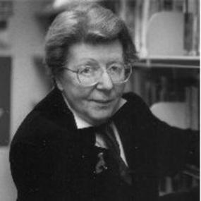 Black and white, head-and-shoulders photo of U. A. Fanthorpe. She has short hair, and wears large-rimmed glasses, and a dark jacket or sweater with a dog brooch over a white shirt.