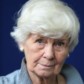 Colour photo portrait of Jane Gardam at an Edinburgh International Book Festival photocall, 14 August 2013. She wears a blue shirt, has short
            white hair, blue eyes, and is set against a darker blue backdrop. 