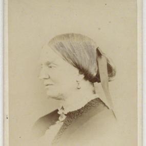 Faded sepia head-and-shoulders photo of Margaret Gatty in profile. Her smooth hair is gathered at the nape of her neck and her eyes cast down. Her dress is dark, with lace at the collar and bust, and she wears drop earrings.