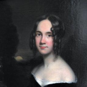 Half-length painting of Sarah Josepha Hale by James Reid Lambdin, c. 1831. She stands at a slight turn against an outdoor nighttime scene, wearing a black dress that sits low on her shoulders, with white at the neckline. Her dark hair, pulled back, hangs in ringlets around her face.