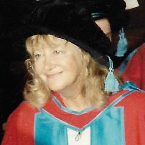 Colour photograph of Sylvia Kantaris in academic dress when she received an honorary D.Litt. from Exeter University. Her gown is red, with light blue and white in the hood, her cap black with a light blue tassel, her hair shoulder-length and blonde.