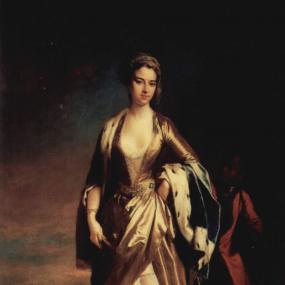 Photo of a full-length painting of Lady Mary Wortley Montagu by Jonathan Richardson recording her time in Turkey. She stands outdoors, with famous buildings of Constantinople (Istanbul) visible beyond. She is dressed in gold: a caftan whose deep V-neck and open skirt reveal a lace shift and long harem drawers. She also wears a gold cap which she calls a talpock on her dark hair, a blue cloak edged with ermine, pearl drop earrings, and pointed slippers. The presence of the young Black boy behind her is start