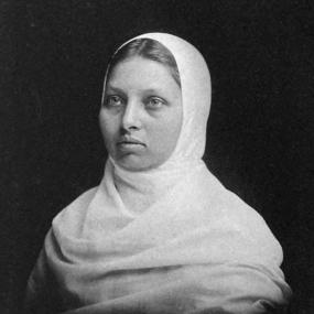 Black and white photograph of Pandita Ramabai, shown from the shoulders up, looking earnestly to the left of the viewer, wearing a white hijab. "Ramabai" is signed below.