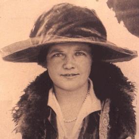 Black and white, head-and-shoulders photo of Margaret Haig, Viscountess Rhondda. She is wearing a white open-neck shirt, dark jacket, fur-trimmed coat, and a large wide-brimmed hat.