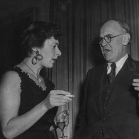 Black-and-white photo of Edith Templeton and V S Pritchett smoking cigarettes as they chat at a party celebrating the 25th anniversary of the
            Book Society, Knightsbridge, London, 1946.