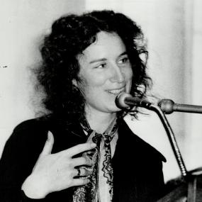 Black-and-white photo of Margaret Atwood standing at a podium and speaking into a microphone, gesturing with her hands, 5 April 1973. 