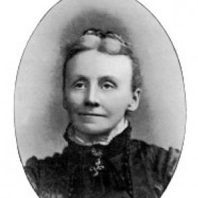 Oval photograph of Matilda Betham-Edwards, c. 1893, looking straight forward with a dreamy smile. She is wearing a high collared dress with a pendant cross, and her hair, grey in front, is arranged tightly on top of her head. Her signature is reproduced below: "Yours truly, M. Betham-Edwards".