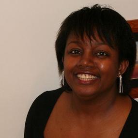 Colour photo of Malorie Blackman looking at the camera, smiling. She is wearing a black V-neck shirt, with three-quarter length sleeves and a pair of dangly silver earrings.
