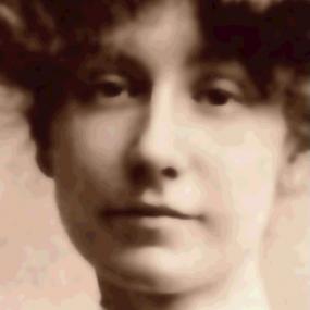 Sepia photograph of Marjorie Bowen. The photograph is tightly focused on her face, which is framed by short but voluminous curls, and she has a lace collar around her neck.