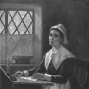Frontispiece of "An Account of Anne Bradstreet The Puritan Poetess, and Kindred Topics", ed. Luther Caldwell (Boston, 1898). Bradstreet is seen sitting at a desk, apparently paused in the act of writing for inspiration from above. She wears a black dress with a coif, big-collared shift, cuffs, and apron all in white.