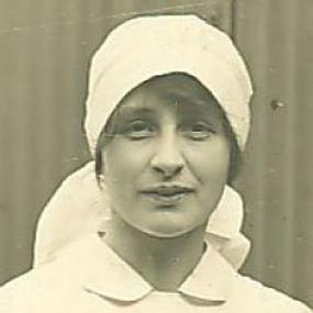 Black and white, head-and-shoulders photo of Vera Brittain, looking straight at the camera, wearing a white shirt and a white scarf wrapped around her head.