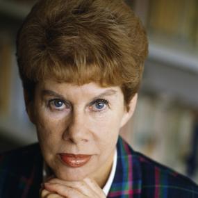 Close-up portrait of Anita Brooker, seated with her hands under her chin, in front of bookshelves at her home in Chelsea, London, 18 September
            1989.