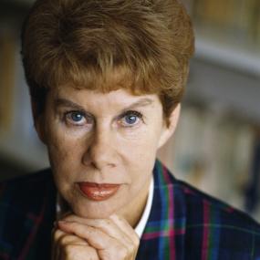 Close-up portrait of Anita Brooker, seated with her hands under her chin, in front of bookshelves at her home in Chelsea, London, 18 September
            1989.