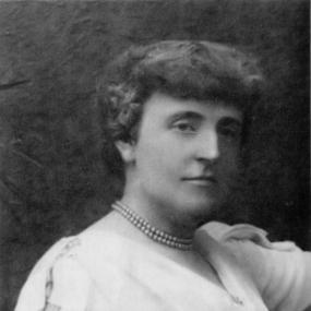 Black and white, head-and-shoulders photograph of Frances Hodgson Burnett, turning to the viewer's right. Her hair is short and she is wearing a pale dress with short sleeves and a double string of pearls around her neck.