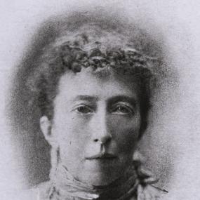Portrait of Agnes Mary Clerke. Black and white portrait of Agnes Mary Clerke. She faces forward with a neutral expression and her hair is short, pulled away from her face. Though the photo appears to be slightly damaged along the bottom, her face and neck are framed and visible. She wears a shirt with a high collar, and what looks like a pendant necklace, though the damage to the photo makes what is on the pendant unclear.