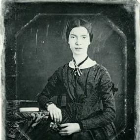 Daguerrotype of Emily Dickinson by William C North, taken sometime between December 1846 and March 1847. She sits with her right elbow on a table beside her, which also a has a book on it. She wears her hair pulled back tight, and a dark gown with touches of white lace, and a ribbon round her neck. Amherst College.