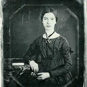 Daguerrotype of Emily Dickinson by William C North, taken sometime between December 1846 and March 1847. She sits with her right elbow on a table beside her, which also a has a book on it. She wears her hair pulled back tight, and a dark gown with touches of white lace, and a ribbon round her neck. Amherst College.
