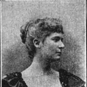 Black and white photograph of Ella Hepworth Dixon. She is shown from the shoulders up, wearing a dark dress with short sleeves. Her hair is in a bun and her head is turned so that her face is in profile.