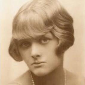 Sepia toned, head and shoulders photograph of the young Daphne Du Maurier. She is wearing a light dress and long string of pearls. Her wavy hair is bobbed, just reaching her jaw, and she has a heavy fringe.