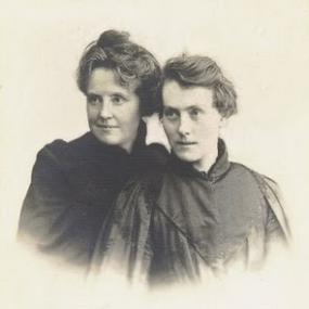 Photo of Michael Field (that is, of Katherine Harris Bradley, left, and Edith Emma Cooper. right) from the waist up, leaning toward each other. They are wearing plain black dresses.