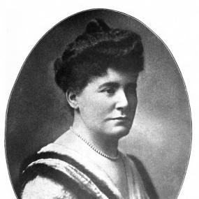 Black and white photograph of Julia Frankau from the bust up. Her dark hair is piled up in a bun; she wears a sleeveless but fur-edged dress and a pearl necklace. Her pseudonym is written below in capitals: "Frank Danby".