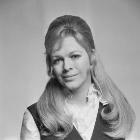 Black-and-white portrait photo of Antonia Fraser, 23 January 1969. She has long blonde hair which is half-up, and wears a white blouse with a
            lacy collar under a dark vest. She has long lower eyelashes. 