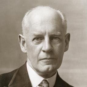 Black-and-white photo of John Galsworthy, full-face, with a serious expression, wearing a dark jacket and a polka-dotted tie.