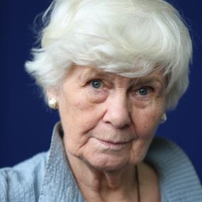 Colour photo portrait of Jane Gardam at an Edinburgh International Book Festival photocall, 14 August 2013. She wears a blue shirt, has short
            white hair, blue eyes, and is set against a darker blue backdrop. 