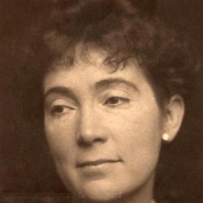 Sepia toned photograph of John Oliver Hobbes, shown from the shoulders up. Her dark wavy hair is pulled back, and she wears small, white, circular stud earrings.