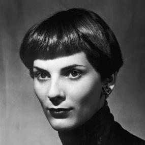 Black-and-white protrait photo of Elizabeth Jane Howard looking off-camera, circa 1956. She wears a dark turtleneck, beaded stud earrings, and
            has short hair that falls above her ear and is cut in bangs.