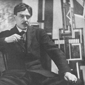 Black and white photo of Wyndham Lewis in London, taken by Alvin Langdon Coburn, 25 February 1916. Lewis is seated, with legs spread wide, holding a cigarette in one hand and resting his other hand on his knee.