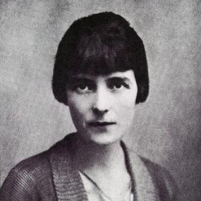 Black and white photograph of Katherine Mansfield, shown from the shoulders up. She is wearing a knitted cardigan with a V-neck and a broad collar, over a light shirt. She has chin-length dark hair and bangs.