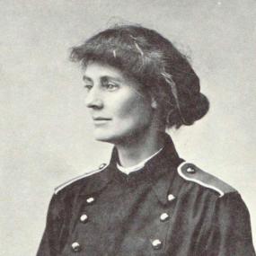 Black and white photograph of Constance, Countess Markievicz, shown from the waist up. She is wearing a military-style double-breasted jacket with a high collar and epaulettes. Her hair is done in a roll in front and a bun behind.