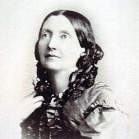 Black and white, head-and-shoulders photograph of Louisa Anne Meredith. She wears a dress with puffed sleeves and a ruffled collar, all in a dark colour, and her hair falls down in dark ringlets.