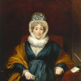 Photograph of a painting of Hannah More by Henry William Pickersgill, 1822. She is seated on a red-upholstered chair beside a little table draped in red fabric and bearing a quill pen, inkwell, and piece of paper. She wears a blue-green mantle with V neck and creamy fabric at the cuffs and neckline, finished with a ruff around her neck. She has a gold shawl and a cap topped with pale blue ribbons. More wrote that she was "condemned, sorely against her will," to sit for this portrait. The version here, in th
