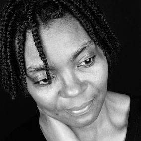Black-and-white close-up portrait of Joan Riley, in which she wears dreadlocks and a dark shirt, 11 February 1997. 