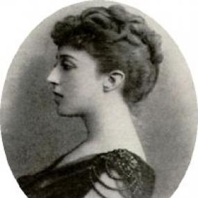 Black and white, head-and-shoulders photo of Martin Ross, seen in profile. She wears a dark, sleeveless evening dress with beading at the shoulder, and her dark, curly hair in a pleat on her head..
