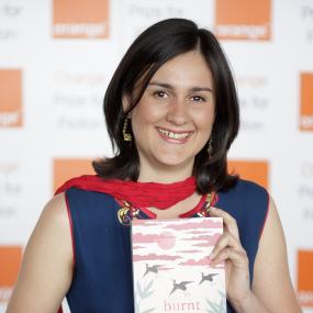 Colour photo of Kamila Shamsie, standing and holding her book Burnt Shadows during the Orange Prize for Fiction event at the Royal Festival
            Hall in London, 3 June 2009.