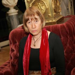 Photo of Penelope Shuttle during the T.S Eliot prize-giving at the Wallace Collection in London, 15 January 2006. She is seated on a red
            velvet couch and wears a red scarf with tassels.