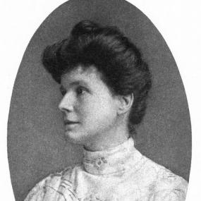 Oval black and white, head-and-shoulders photograph of May Sinclair in semi-profile, c. 1912. She is wearing a white, embroidered dress or blouse with a high collar; her dark hair is pulled up in a loose roll with a bun on top.