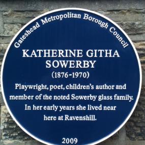 Photograph of a round blue plaque dedicated to Githa Sowerby by Gateshead Metropolitan Borough Council, set in a grey stone wall. The council's name appears at the top, followed by: Katherine Githa Sowerby (1876-1970). Playwright, poet, children's author and member of the noted Sowerby glass family. In her early years she lived near here at Ravenshill." At the bottom the plaque is dated 2009.