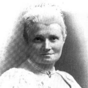 Black and white, head-and-shoulders photograph of Flora Annie Steel looking straight at the viewer. She is wearing a light dress with little visible below the neckline, and a necklace with two stones in its centre. Her probably grey hair is brushed back.