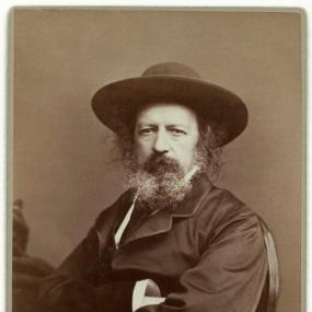Albumen cabinet card, created late 1860s by Elliott &amp; Fry, of Tennyson seated in a chair with arms crossed, looking at the camera, wearing a at.