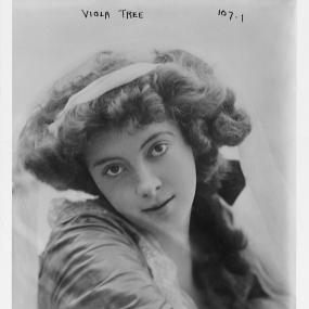 Black and white, head-and-shoulders photograph of Viola Tree. Her head is tilted with a winsome expression. She wears a gauzy top and has her hair in thick, bulky curls at the sides and tied at the back.