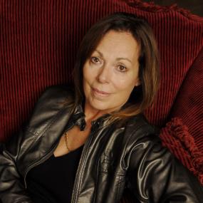 Colour photo of Rose Tremain promoting her writing at an event in Paris, France, 27 February 2007. Looking off-camera, she sits on a red and
            black striped couch and wears a black leather jacket.