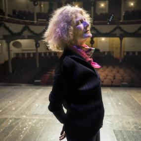 Colour photo of Timberlake Wertenbaker onstage at Ford's Theatre, in Washington, DC, 29 December 2017. Shown in profile and backlit, her hands
            are clasped behind her back and her eyes are closed. 