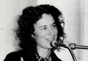 Black-and-white photo of Margaret Atwood standing at a podium and speaking into a microphone, gesturing with her hands, 5 April 1973. 